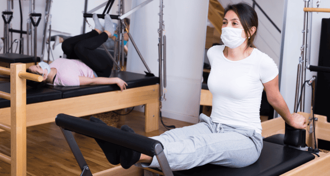 A woman wearing a mask and using a reformer